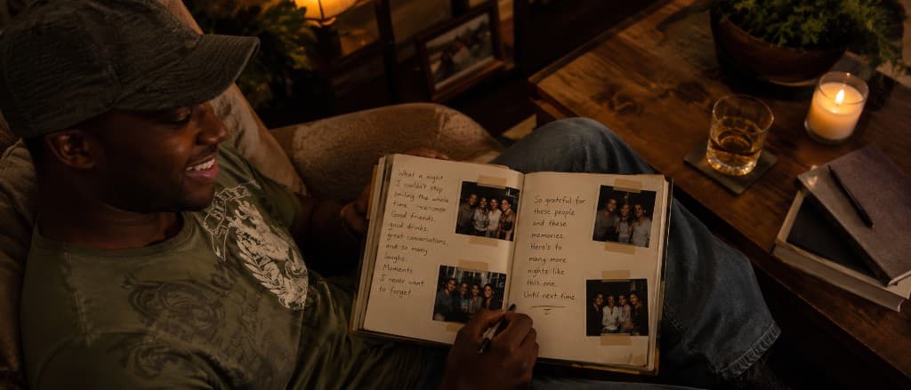 A person writing in a physical journal by candlelight, photographs taped to the pages — the night remembered in your own hand.